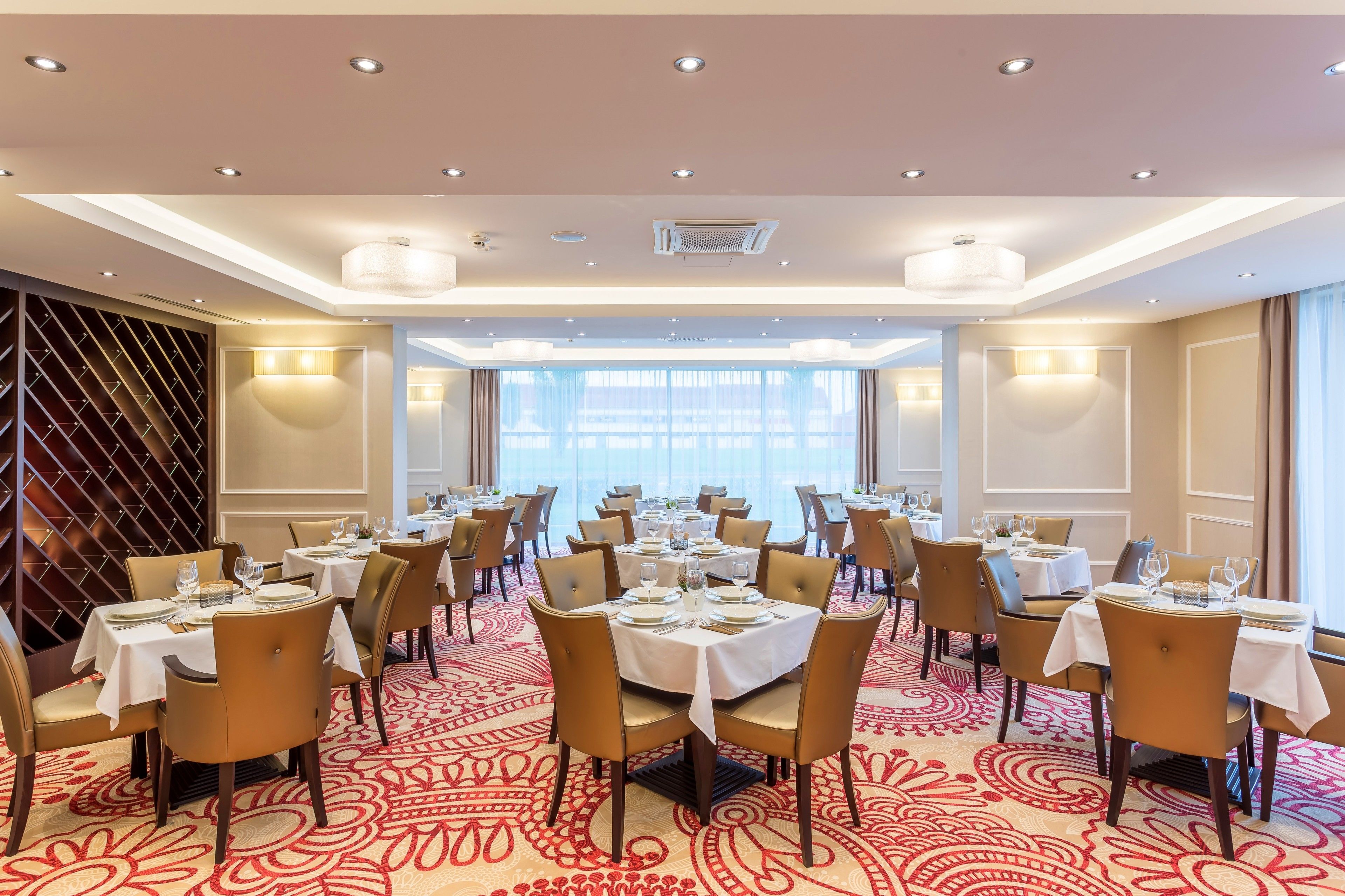 A hotel dining area with multiple round tables set for dining, equipped with white tablecloths and gold chairs.