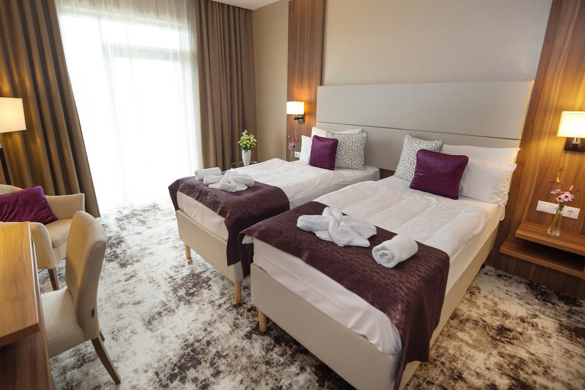 A hotel room with two beds, a chair, a desk, and a large window with curtains.