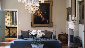 Een woonkamer met een pronkstuk, een bank, een kussen in de vorm van een hond, en een schilderij aan de muur.