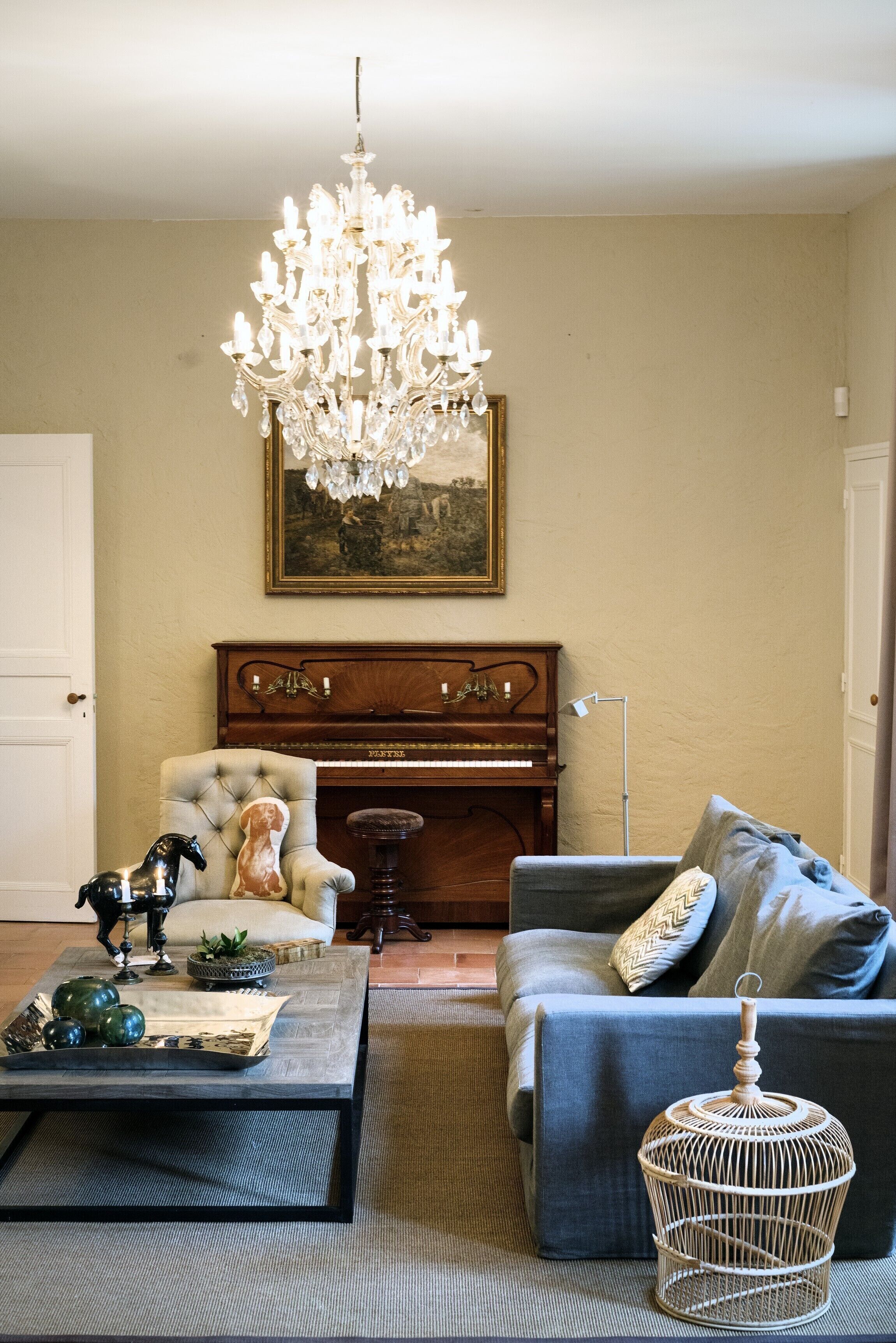 A living room with a grand chandelier, a piano, a sofa, and a coffee table.