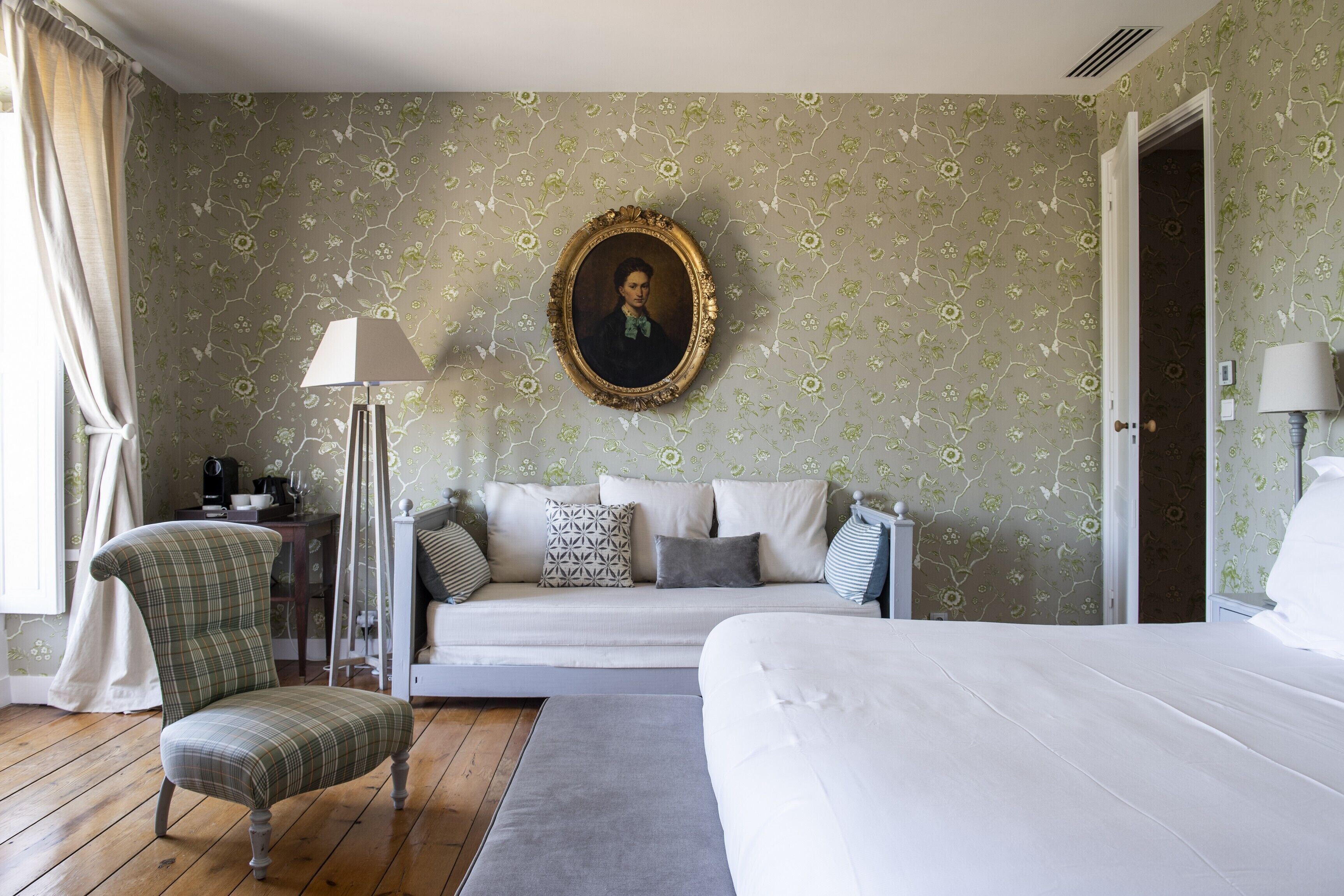 A bedroom with a bed, a sofa, a chair, a painting on the wall, and a door.