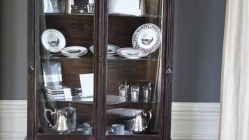 Et mørkt træskab med glaslåger, der viser porcelæn, drikkeglas og bøger.