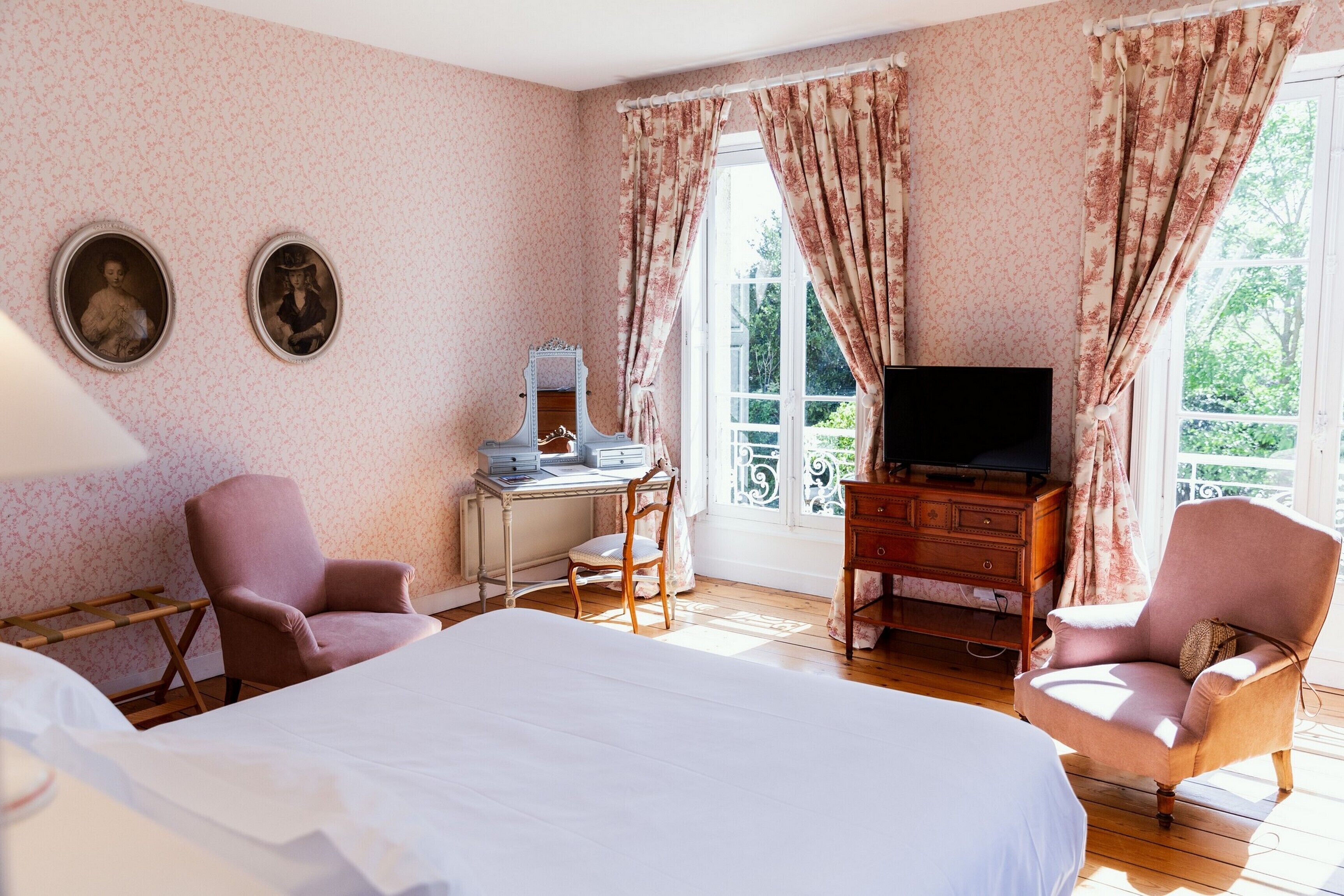Une chambre d’hôtel comprenant un lit, deux fauteuils, un bureau avec un ordinateur, une télévision et une fenêtre avec des rideaux.
