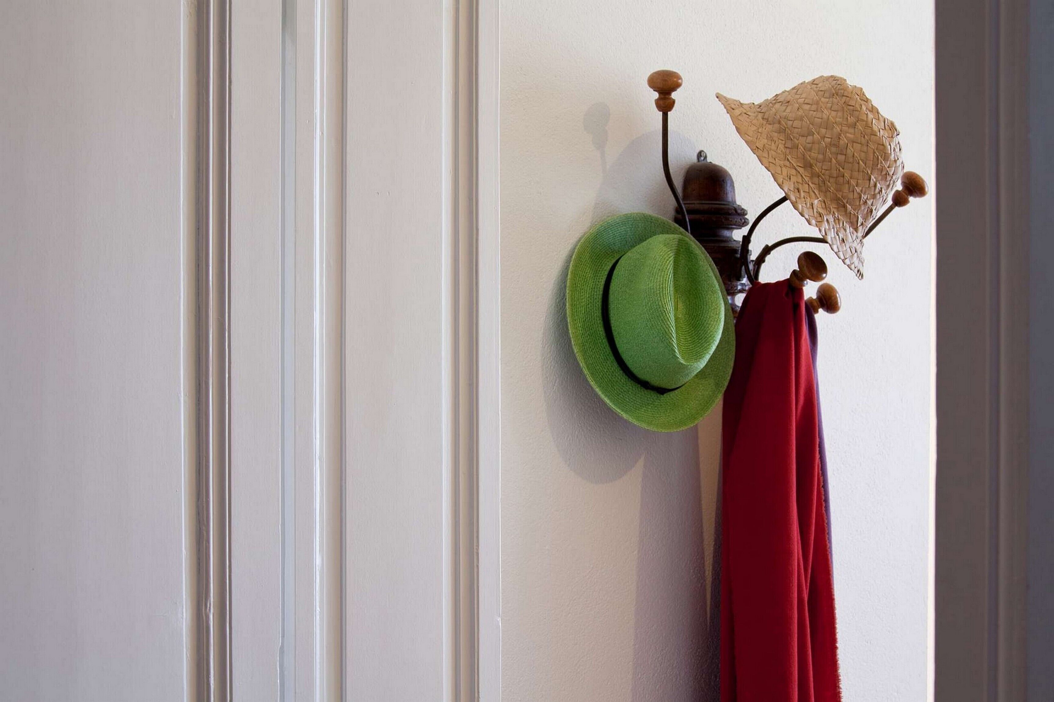 Un perchero de pared con un sombrero verde y una prenda roja.