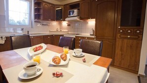 A breakfast setup with croissants, coffee, and orange juice on a table in a kitchen with wooden cabinets and a microwave. - Penzion Olomouc (Olomouc)