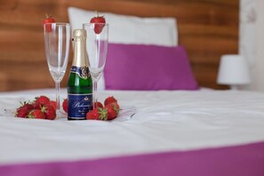 Ein Bett mit einer Champagnerflasche und zwei Gläsern, jeweils mit einer Erdbeere.