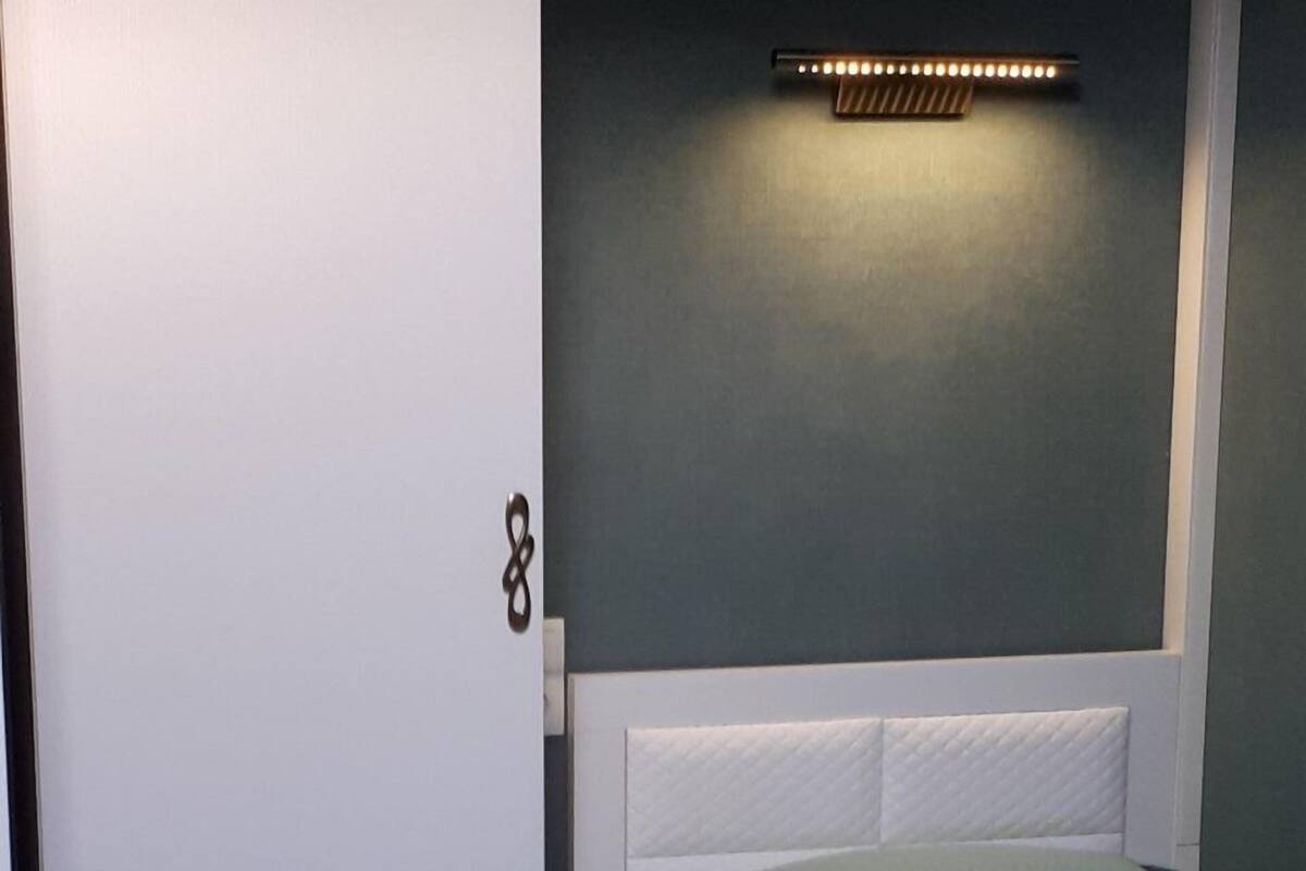 Un dormitorio con una cama, cabecera blanca, una lámpara de pared y una puerta con manija.