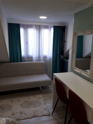 A room with a sofa, a desk, a chair, a mirror, and a window with curtains. - Nicolas (Tbilisi)