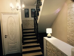 A staircase with a white door, a wall with framed pictures, and a lamp on a white table. - Nicolas (Tbilisi)