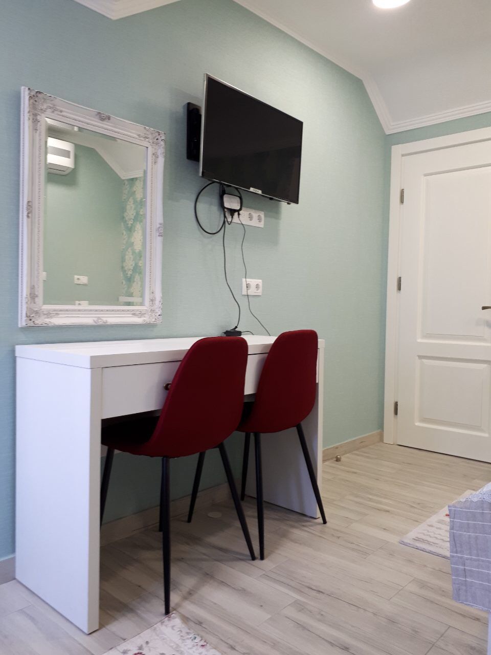 A room with a white desk, two red chairs, a mounted TV, and a door.