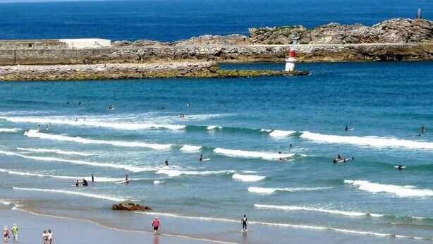 A coastal beach scene with waves, a lighthouse, and rocky outcrops. - Hotel Playa de Merón (San Vicente de la Barquera)