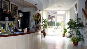 A reception area with a counter, potted plants, and framed pictures on the wall. - Hotel Playa de Merón (San Vicente de la Barquera)