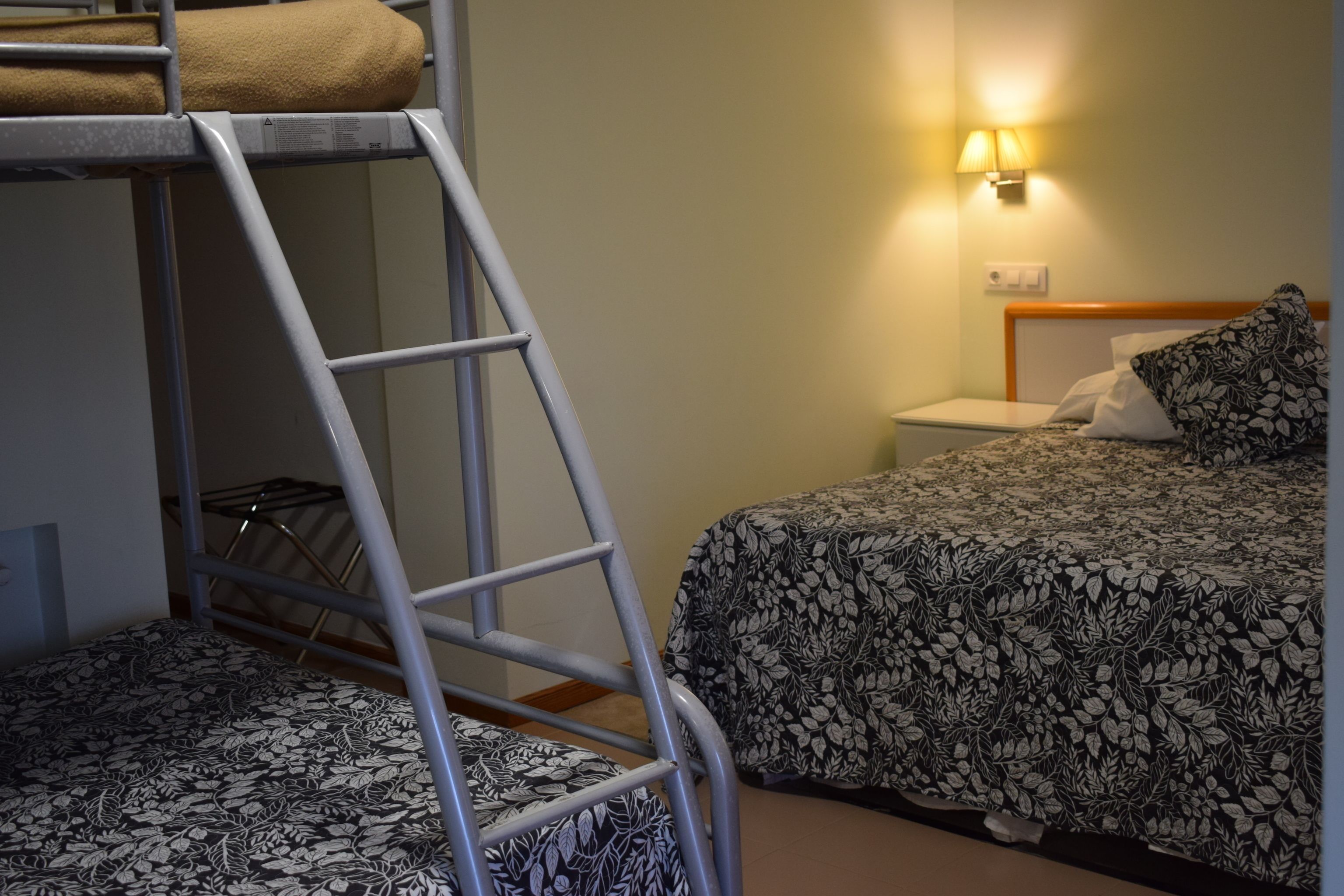 A bunk bed with a ladder, a bedside table with a lamp, and a floral-patterned bedspread.