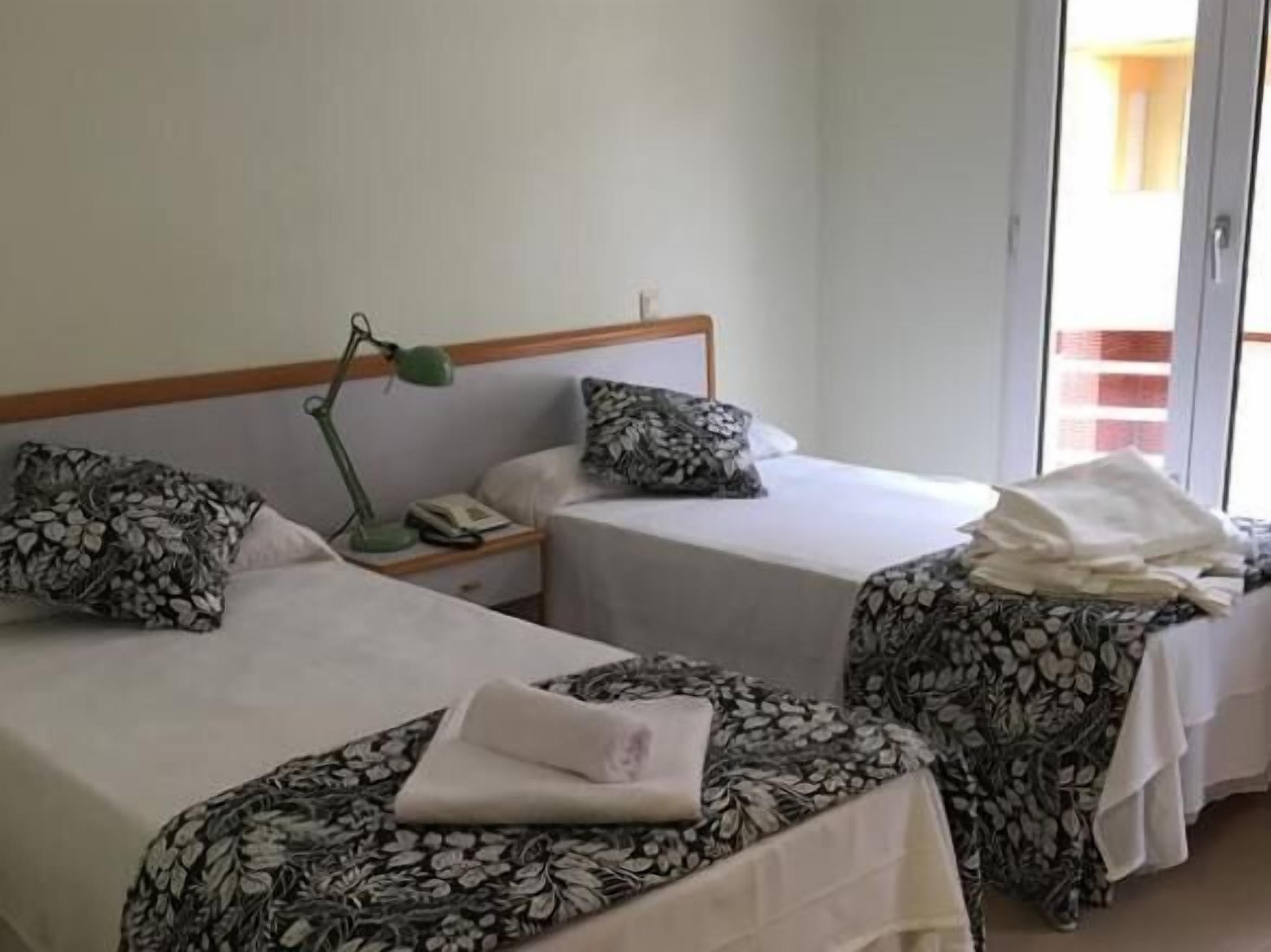 A hotel room with two beds, each with a patterned bedspread, a bedside lamp, and a pillow.