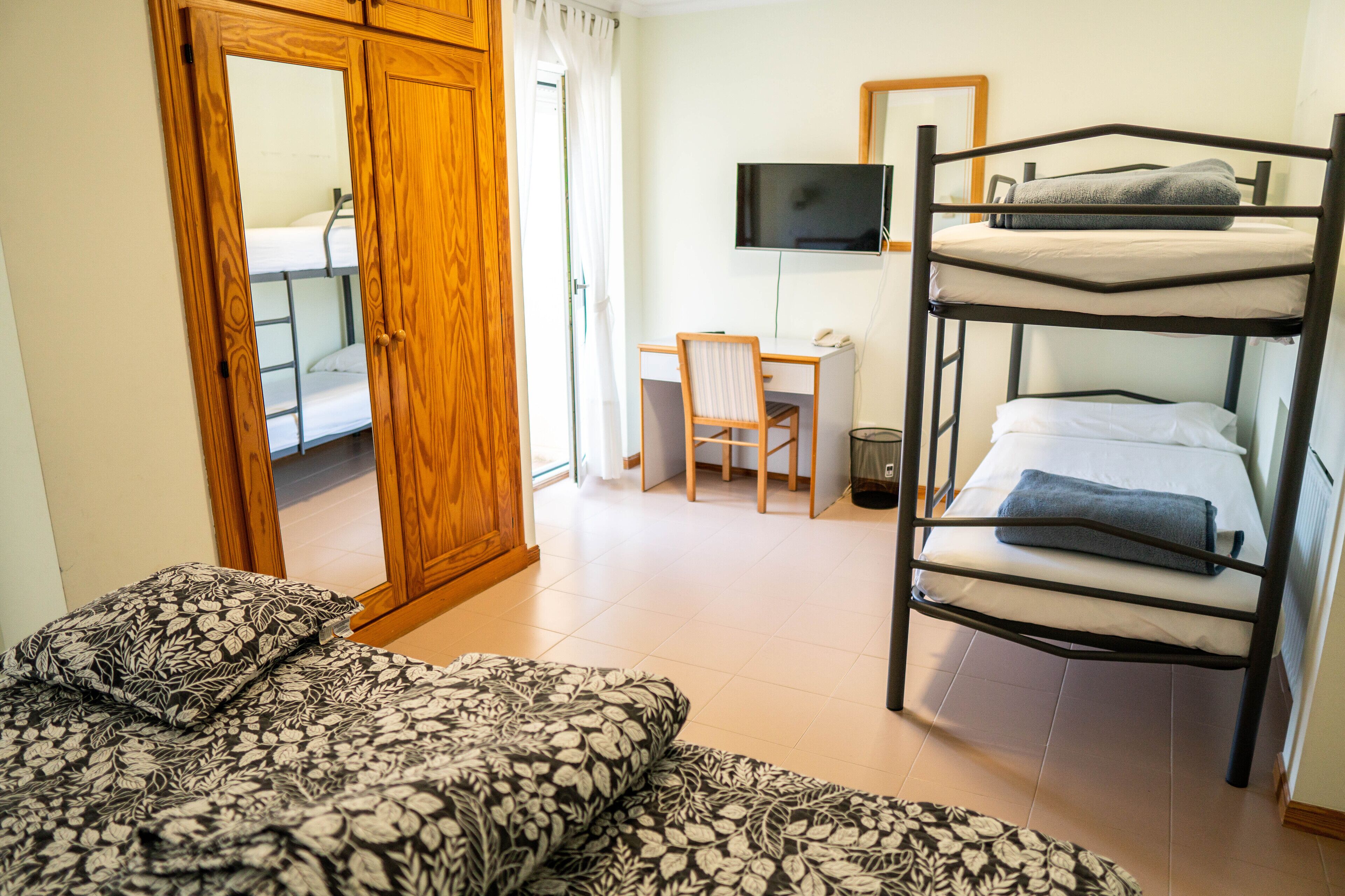 A dormitory room with bunk beds, a desk, a chair, a television, and a wardrobe.