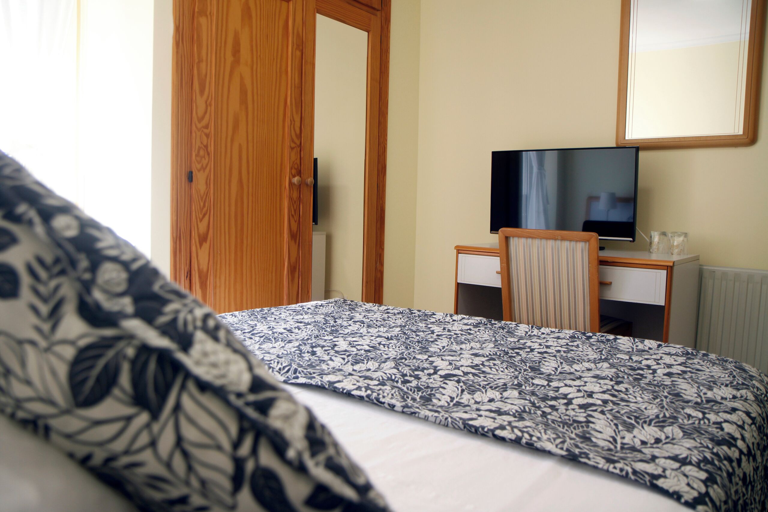 Une chambre d’hôtel avec un lit, un bureau, une chaise, une télévision et une fenêtre.