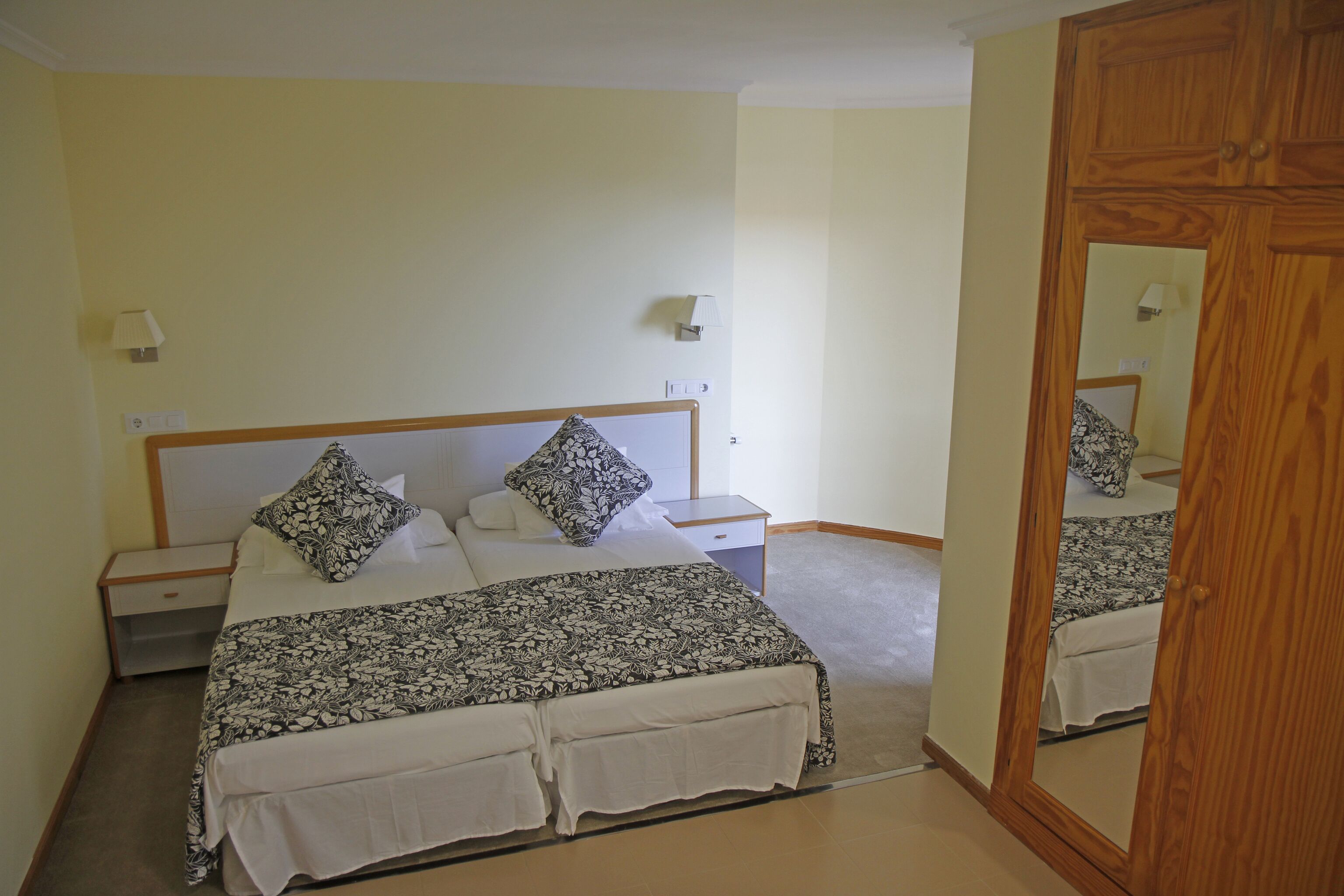 A bedroom with a bed, nightstands, a mirror, and a wall-mounted lamp.