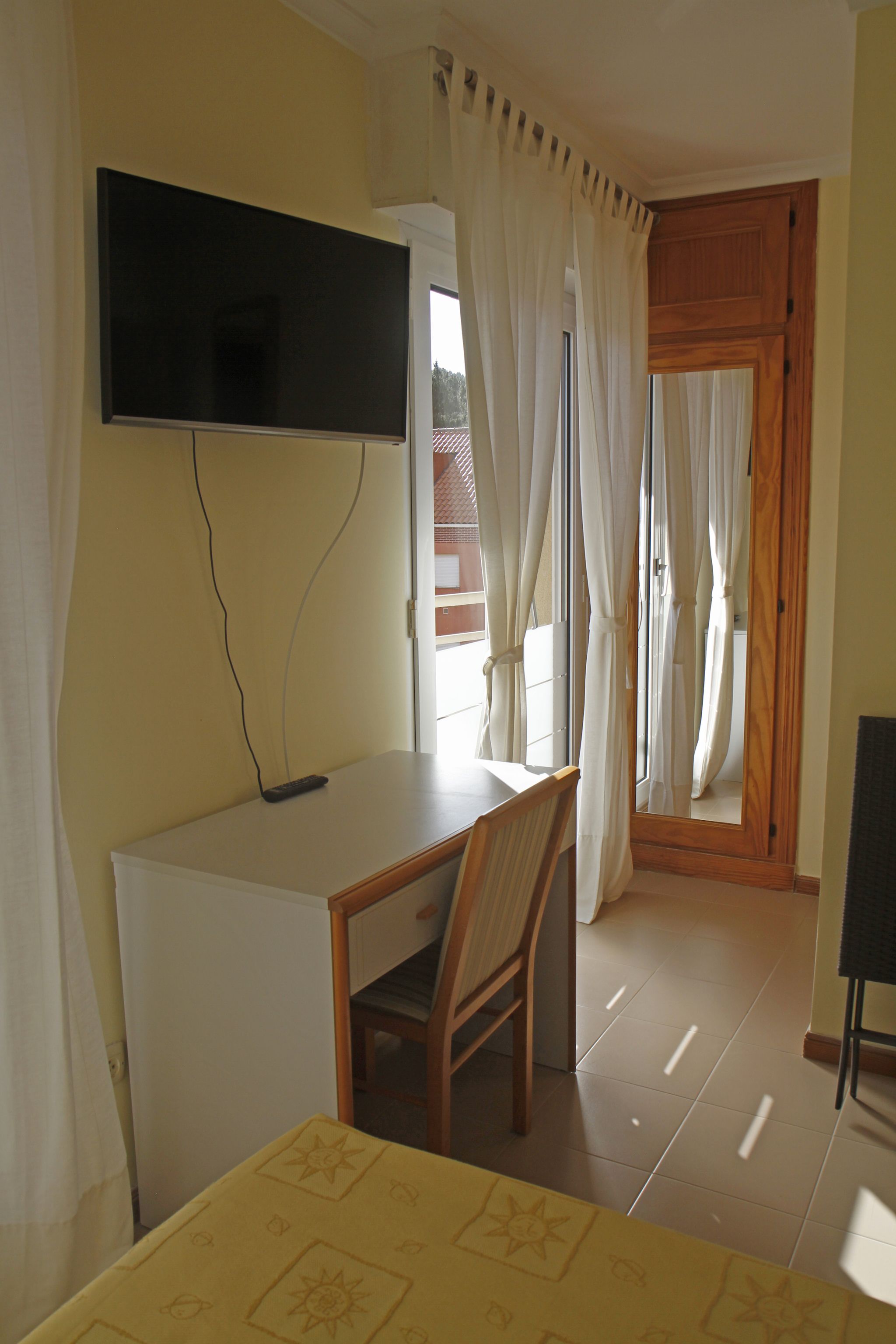 A room with a desk, chair, and a television mounted on the wall.