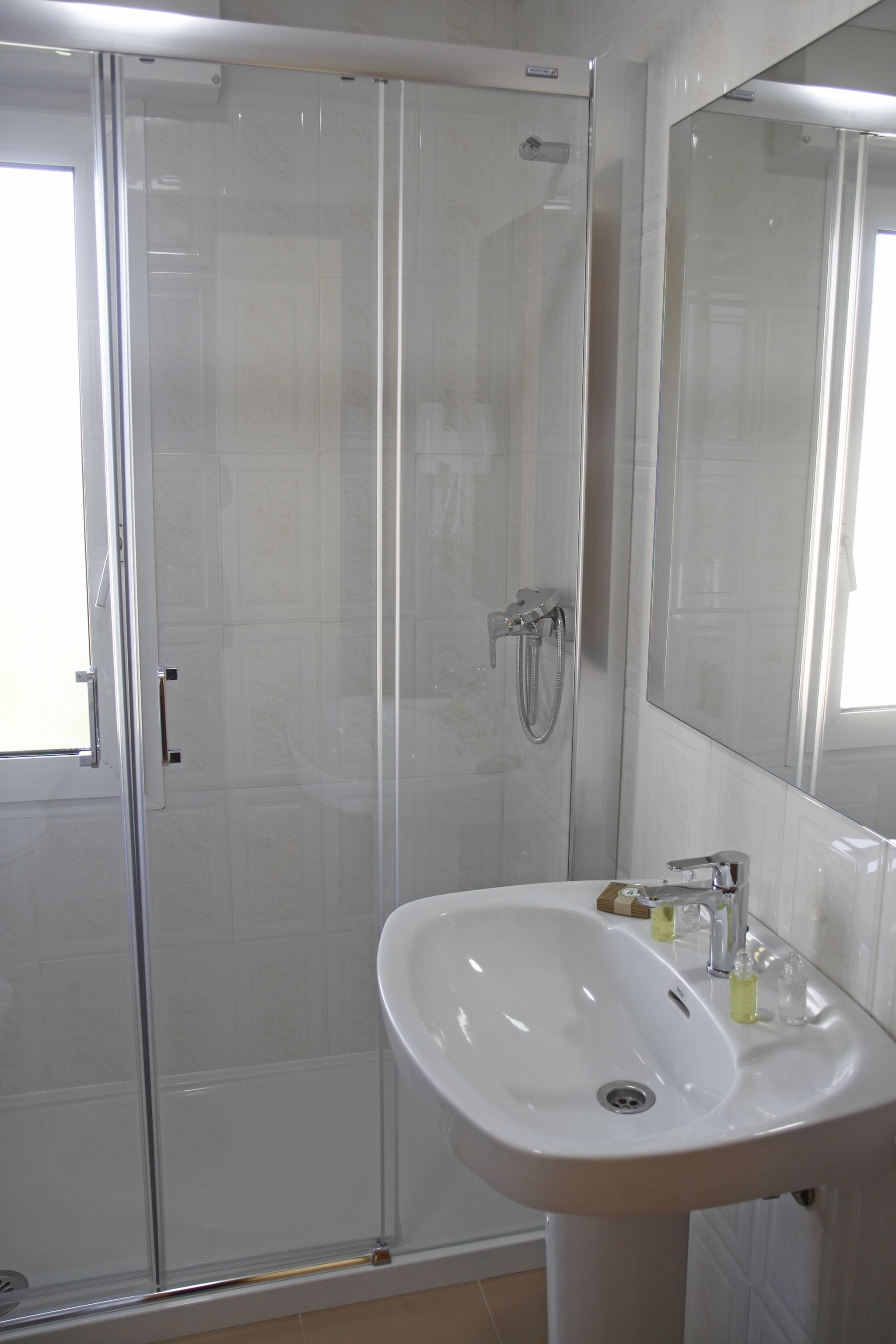 A bathroom with a glass-enclosed shower, a white sink, and a large mirror.