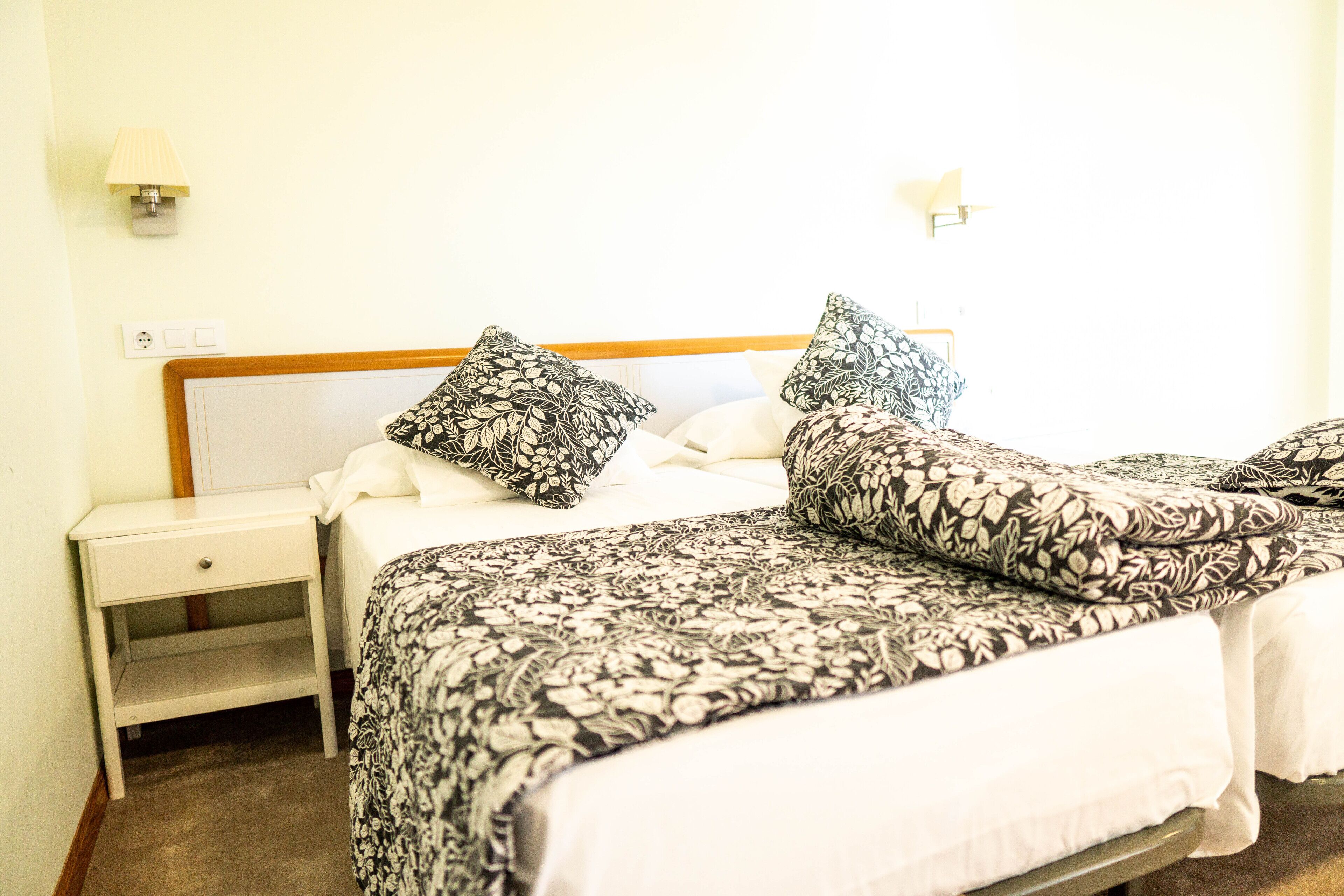 A hotel room with a bed, two pillows, a nightstand, and a lamp.