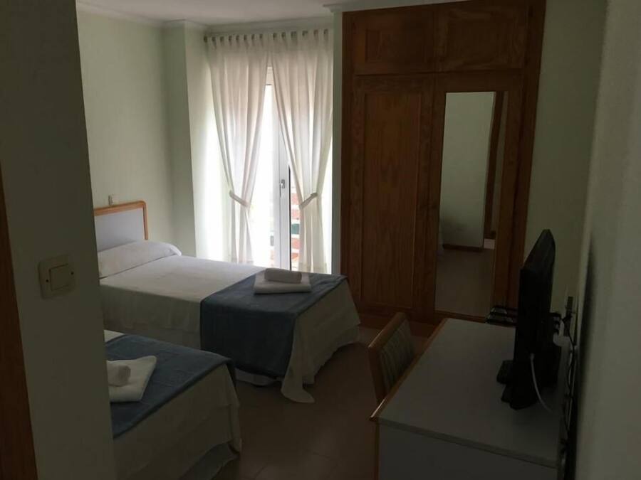 A hotel room with two beds, a desk, a chair, a television, and a wardrobe.