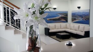 A reception area with a vase of white flowers, a reception desk, a modern sofa, and a staircase. - Hotel Playa de Merón (San Vicente de la Barquera)