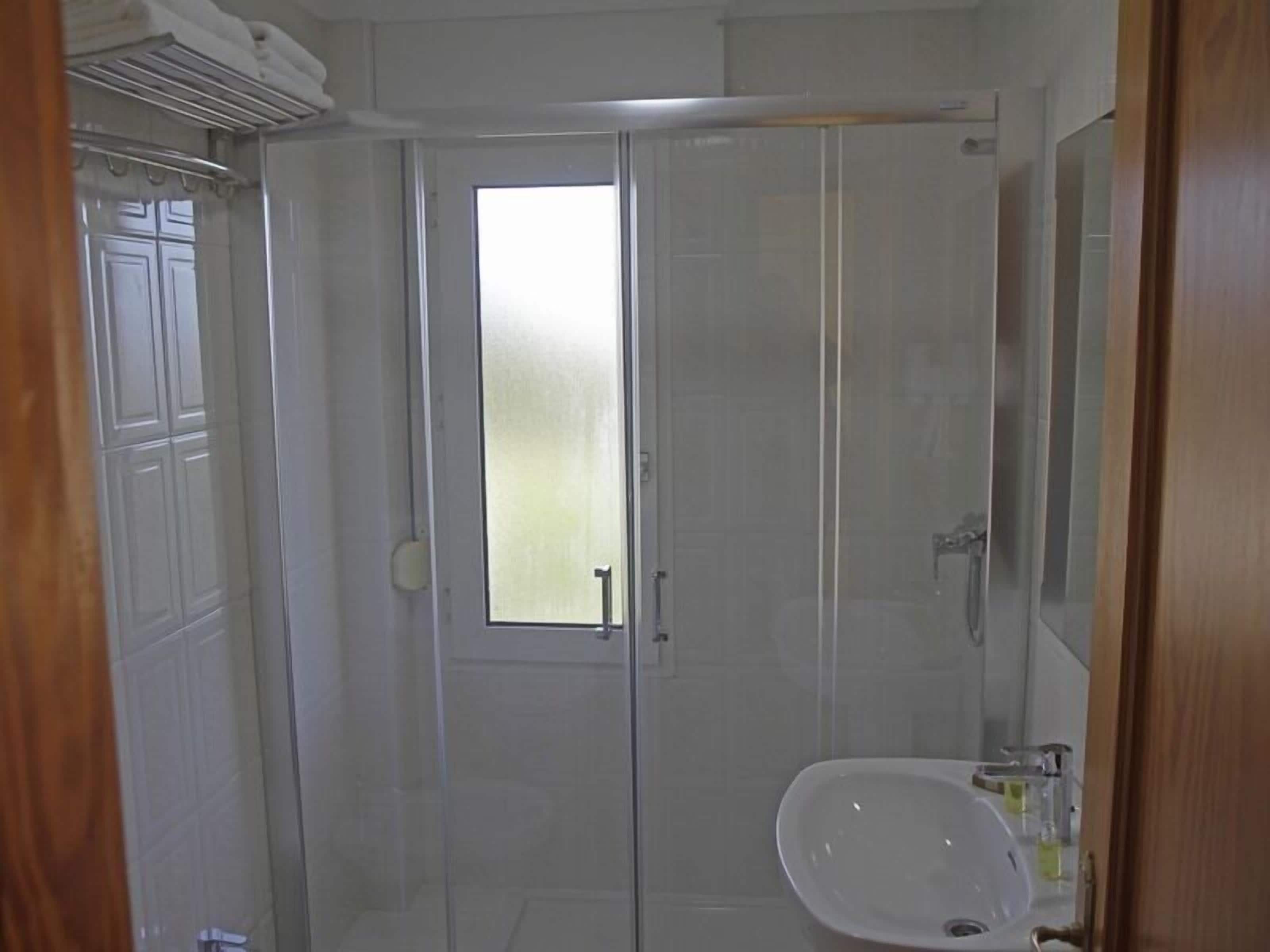 A bathroom with a glass shower enclosure, a sink, and a mirror.