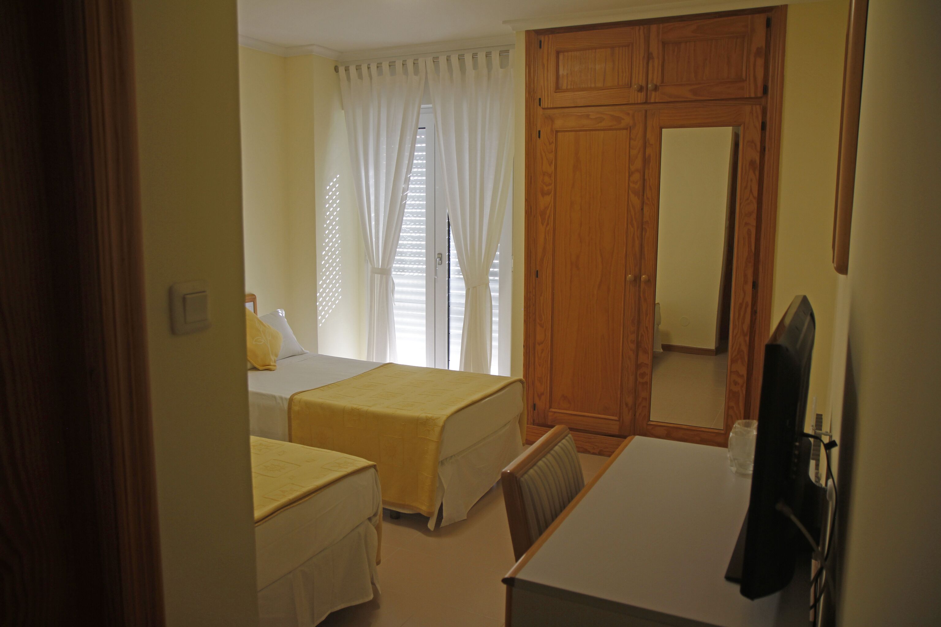 A bedroom with two beds, a desk, a mirror, and a wardrobe.