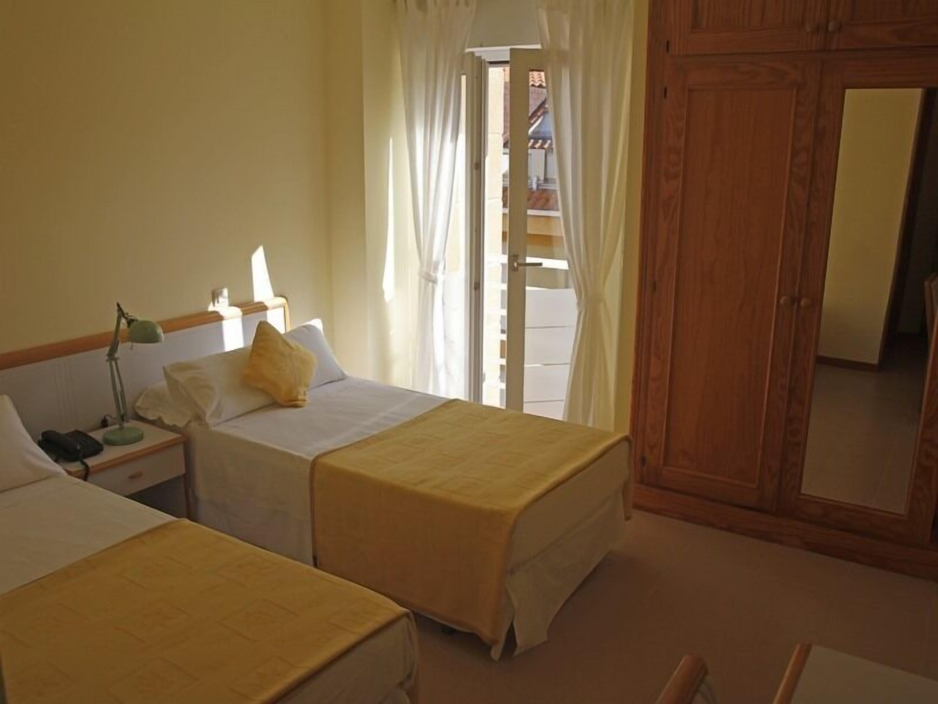 A hotel room with two beds, a nightstand with a lamp, a telephone, and a window with curtains.