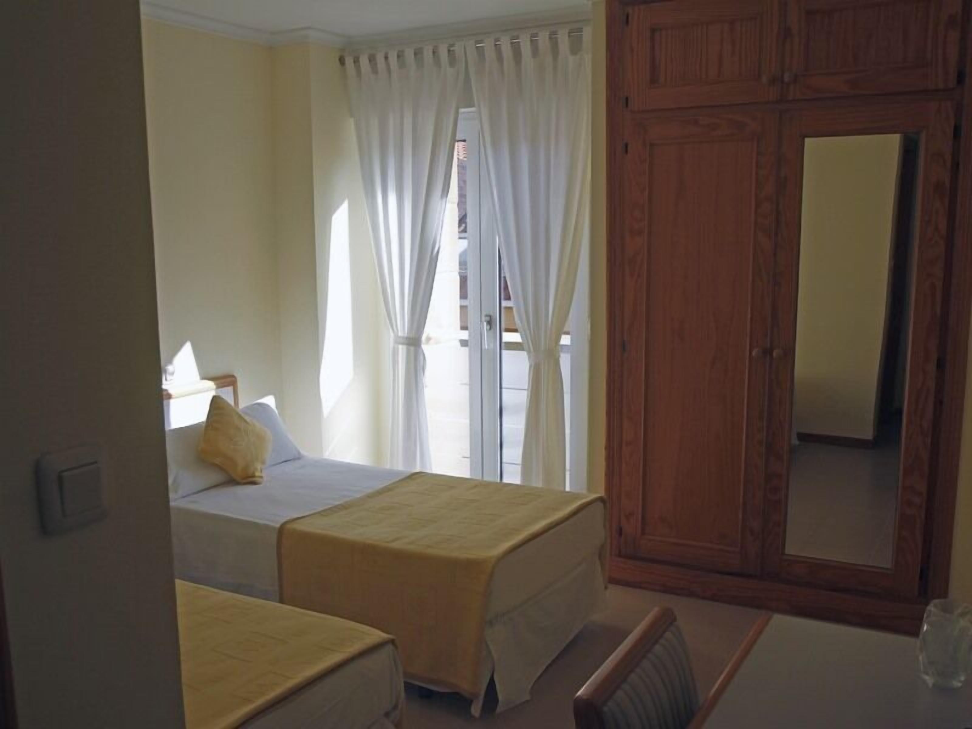 Une chambre avec deux lits, une armoire en bois et une petite table.