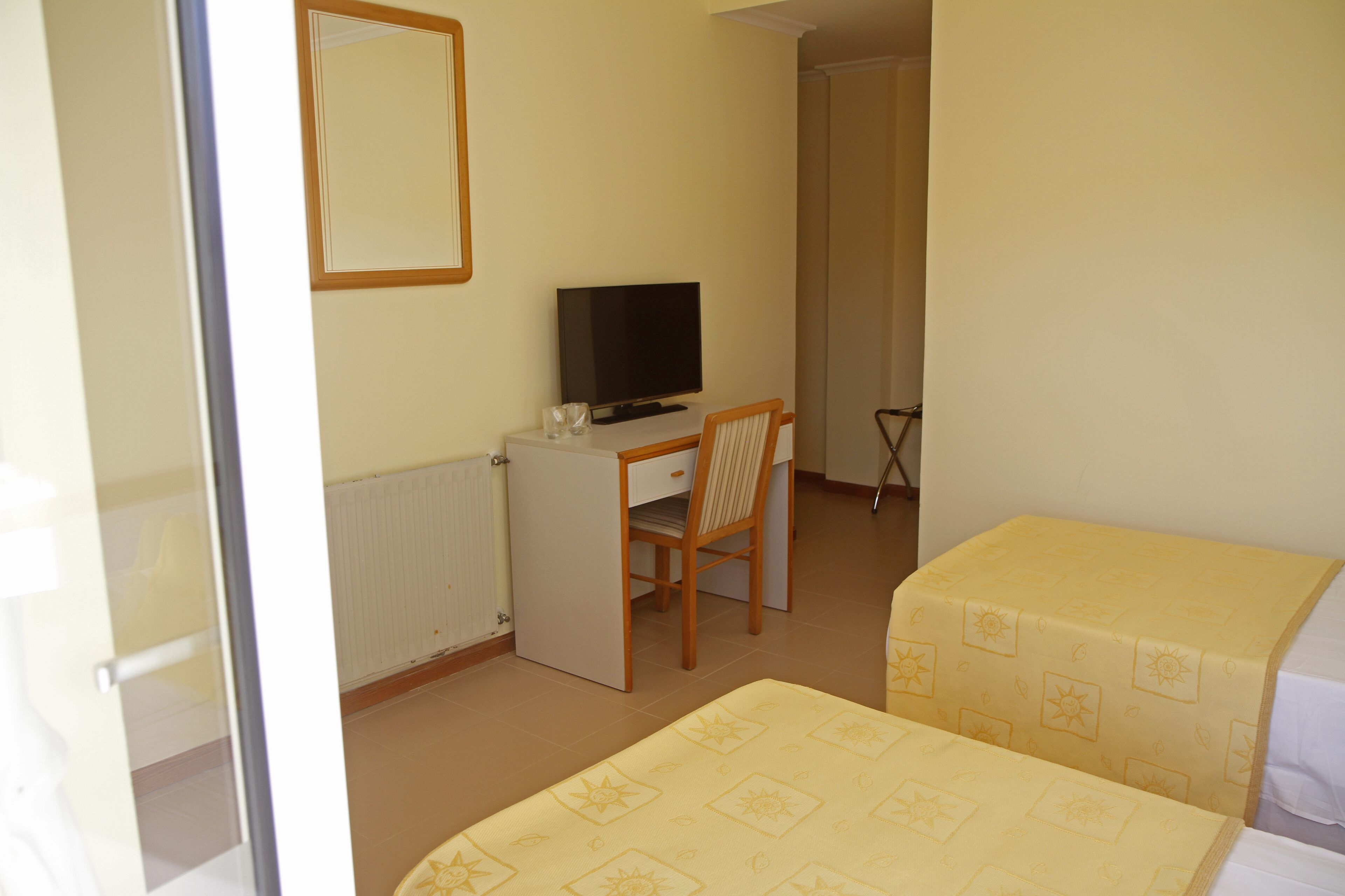Una habitación pequeña y limpia con una cama, un escritorio con una silla, un televisor y un radiador.