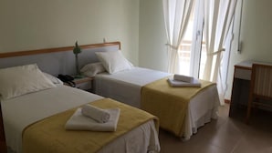 A hotel room with two beds, each with a yellow bedspread and white pillows. There is a bedside table with a lamp and a phone. The room has a window with sheer curtains and a view of the outside. - Hotel Playa de Merón (San Vicente de la Barquera)