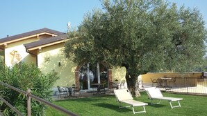 A building with a yellow facade, outdoor seating area, and a large tree providing shade. - B&B Al Cristo (Sant'Ambrogio di Valpolicella)