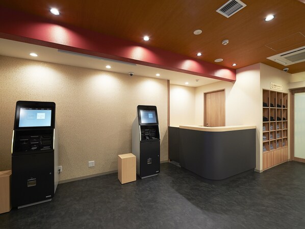 A reception area with two self-service kiosks, a wooden reception desk, and a storage unit with folded items. - The Pocket Hotel Kyoto Shijokarasuma (Kyoto)
