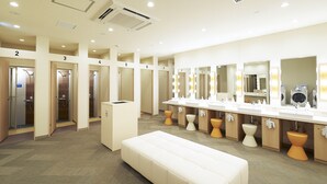 A hotel bathroom with multiple shower stalls, a large vanity with mirrors, and a bench. - The Pocket Hotel Kyoto Shijokarasuma (Kyoto)