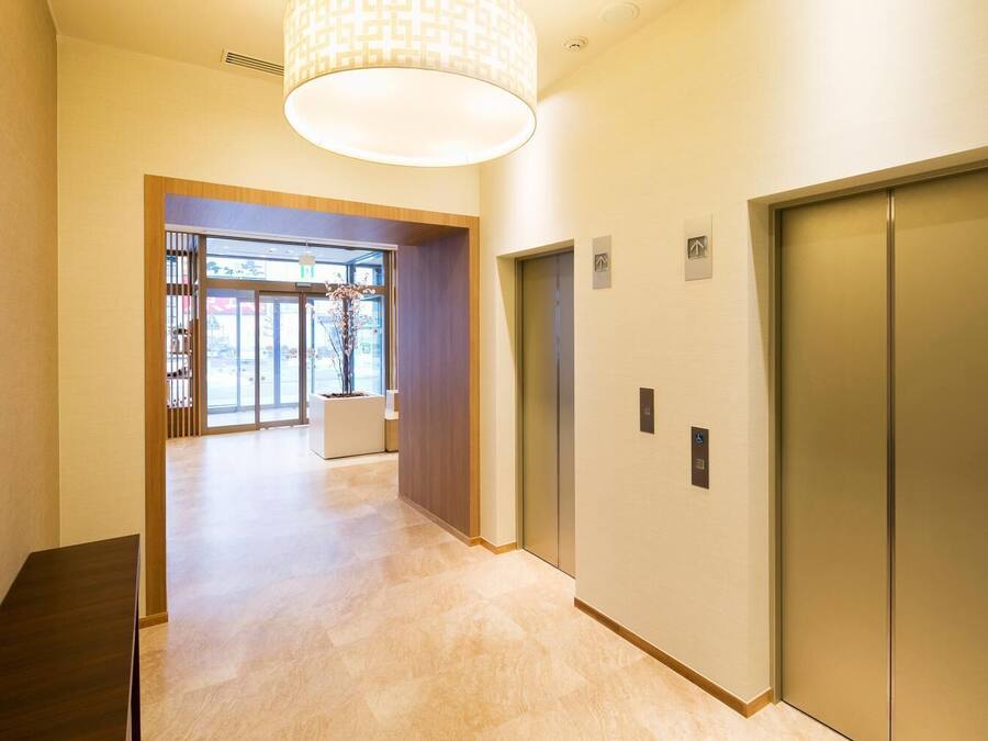 A modern hallway with a wooden bench, a large window, and two elevators.