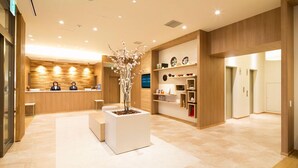 A modern hotel lobby with a reception desk, a central planter with flowers, and a wooden reception area.