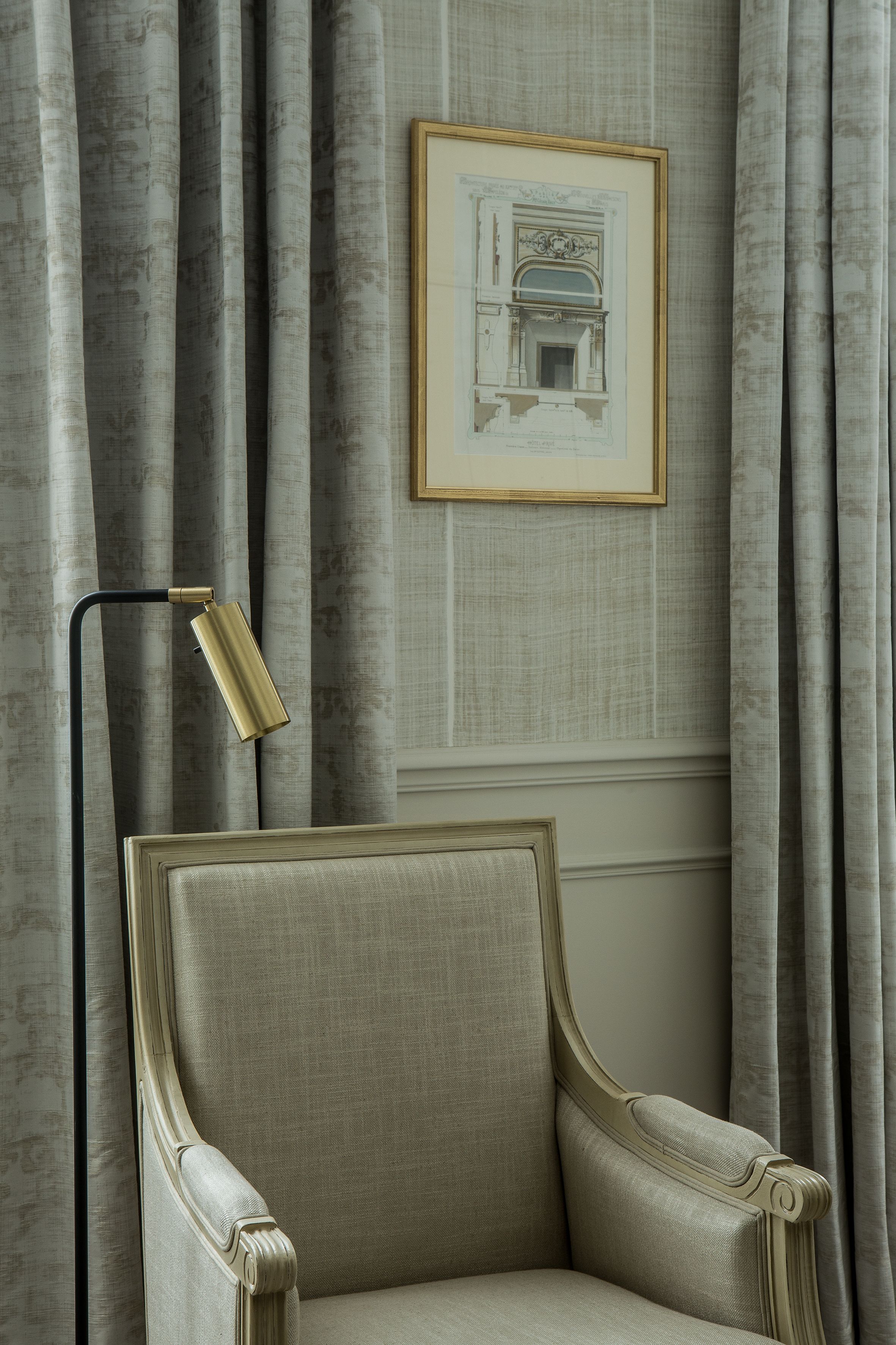 A room with a classic armchair, a framed architectural drawing on the wall, and a floor lamp.