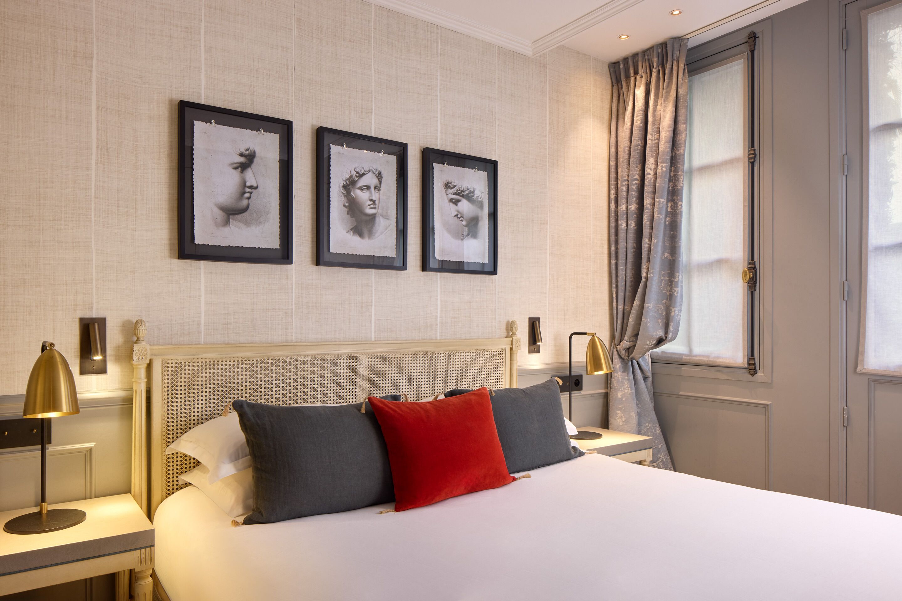 Una habitación de hotel con una cama, dos mesitas de noche, un cabecero y tres cuadros enmarcados en la pared.