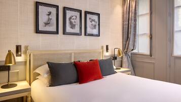 Una habitación de hotel con una cama, dos mesitas de noche, un cabecero y tres cuadros enmarcados en la pared.