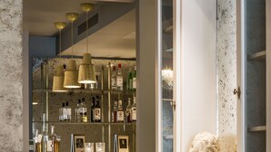 Uma área de bar com balcão, prateleiras cheias de garrafas e luminárias pendentes.