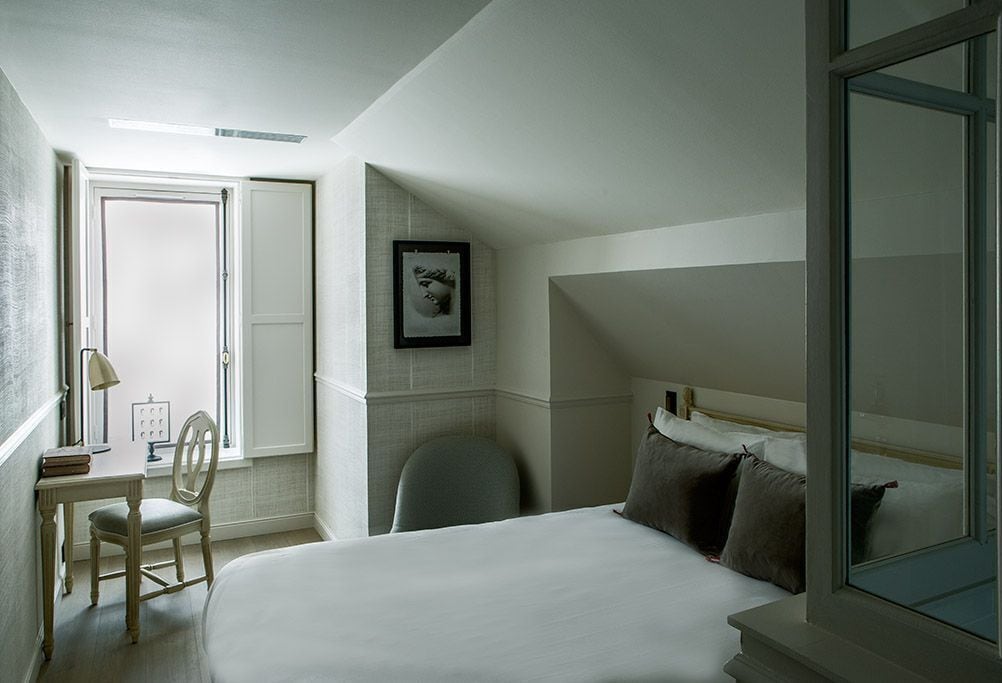 A bedroom with a bed, a desk, a chair, a framed picture on the wall, and a window.