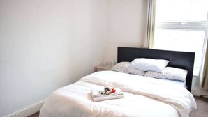 A neatly made bed with white bedding and a folded towel on the footboard.
