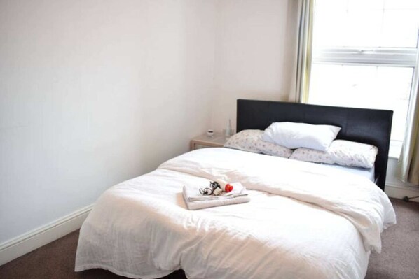 A neatly made bed with white bedding and a folded towel on the footboard.