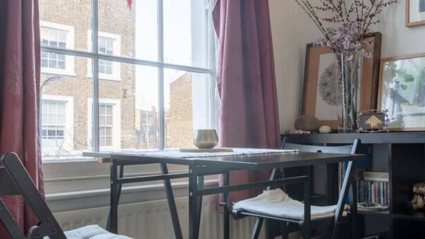 A room with a window, a table, a chair, a bookshelf, and a radiator.