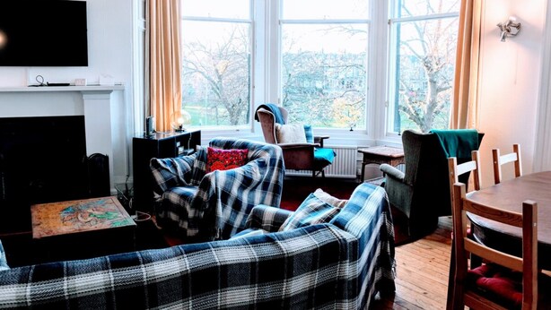 A cozy living room with a plaid sofa, a television, and a window with curtains. - Traditional Apartment oer the Meadows (Edinburgh)