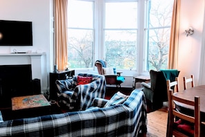 A cozy living room with a plaid sofa, a television, and a window with curtains.