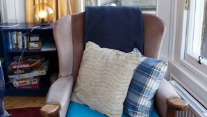 A cozy armchair with a blue cushion and two pillows, positioned near a window with a view of a building. - Traditional Apartment oer the Meadows (Edinburgh)