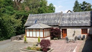A stone house with a tiled patio, a conservatory, and a small garden. - Auchenheglish Lodges - The Smiddy (Alexandria)