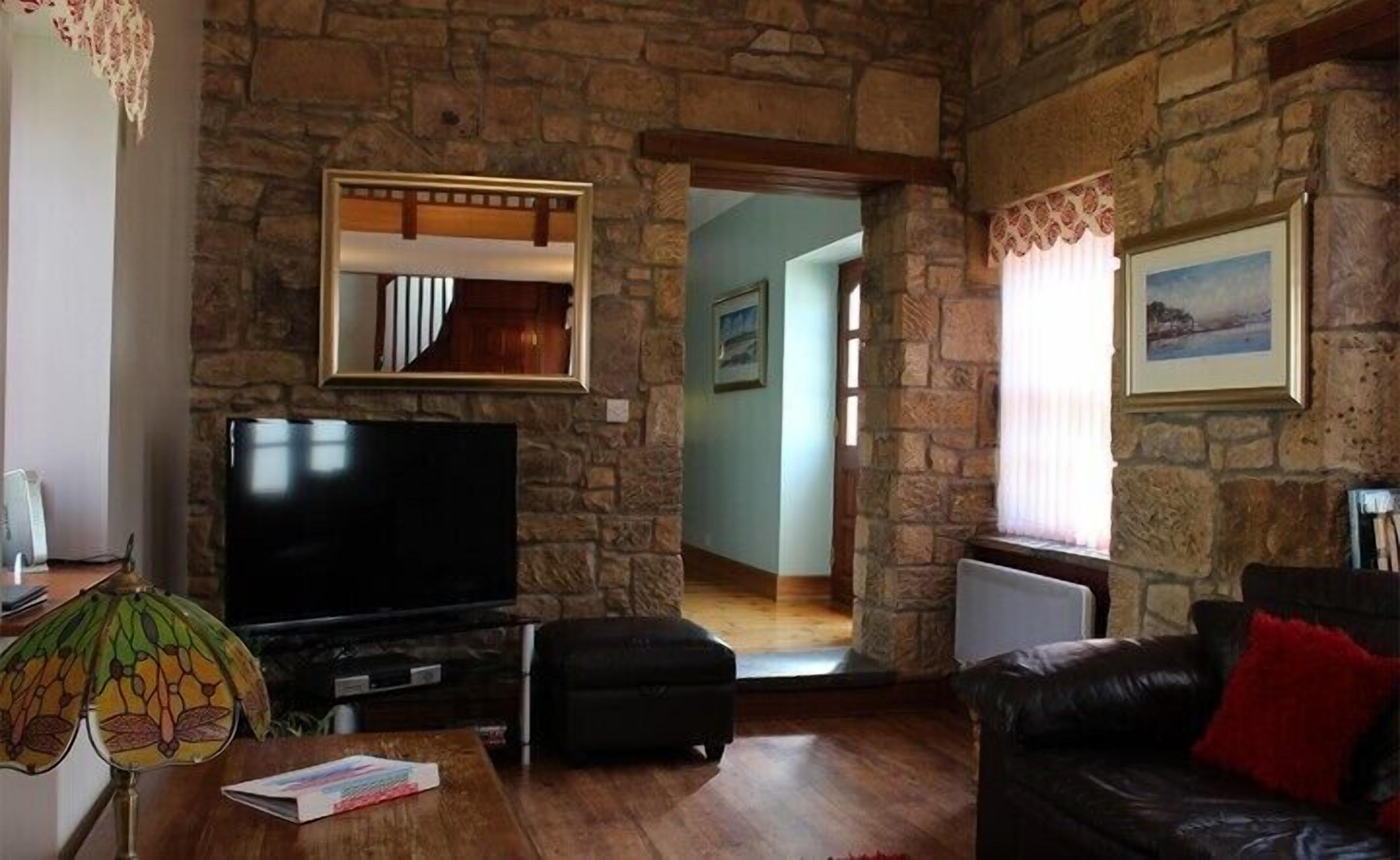 A stone-walled living room with a flat-screen TV, a sofa, and a lamp.